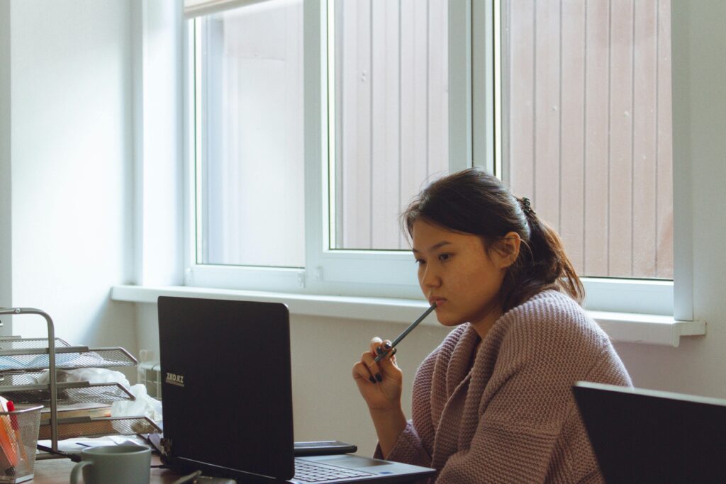 Young woman in cozy sweater working intently on laptop at desk.